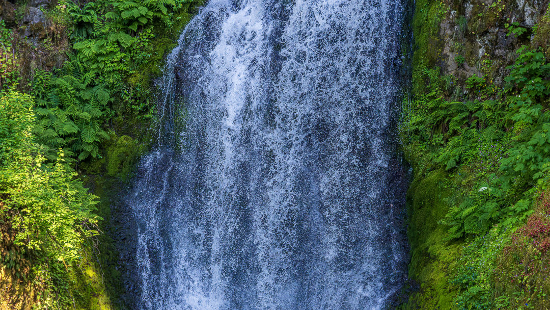 2026_06_12_Waterfalls_00037_3840_thumb ‣ In The Viewfinder Waterfall tumbling down a mossy, rocky cliff framed by lush green foliage.