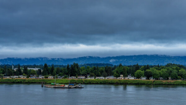 Overcast sky over a river with a tree-lined shore and parked boats along the bank.