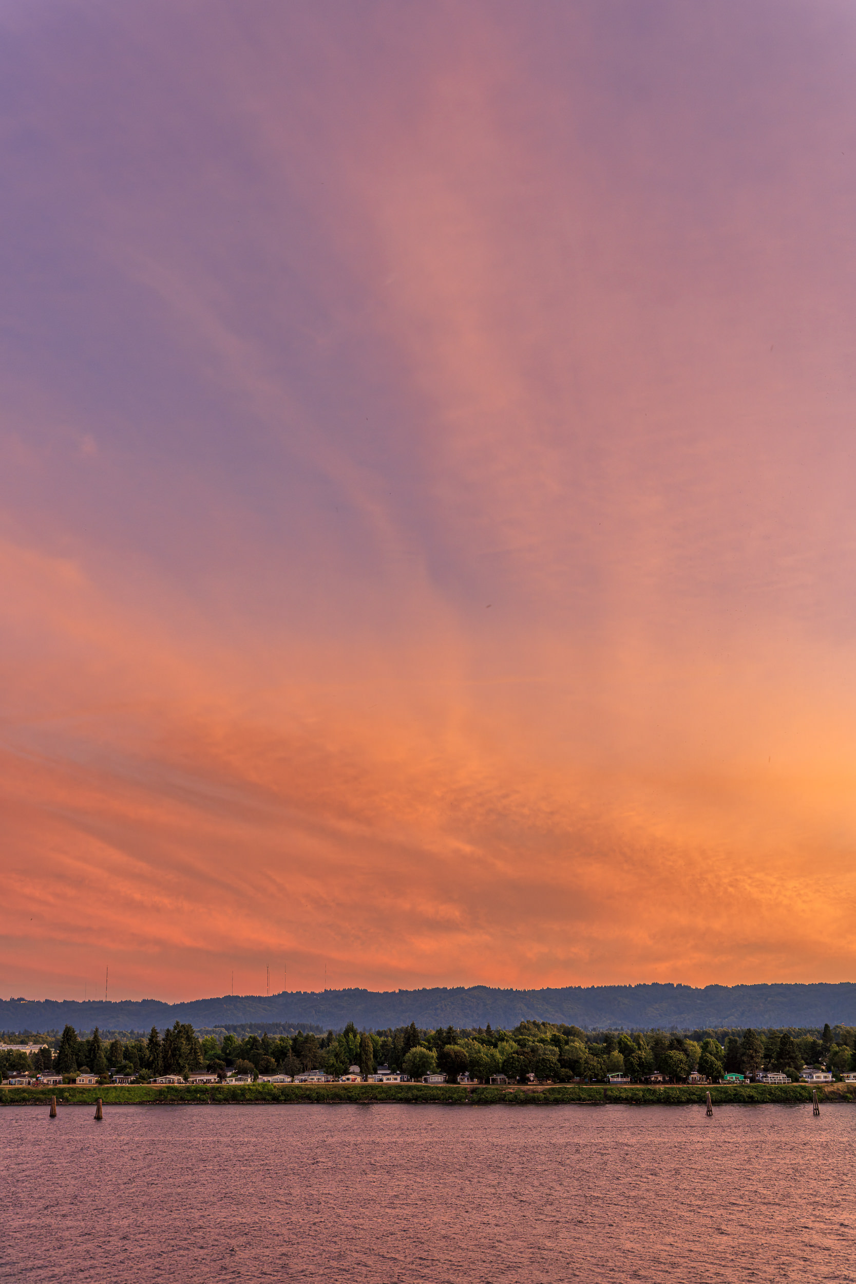 2026_07_19_Balcony_Sunset_0003-Edit_2500 ‣ In The Viewfinder Colorful sunset over a calm body of water, pink and orange sky above a tree-lined shore and distant hills.