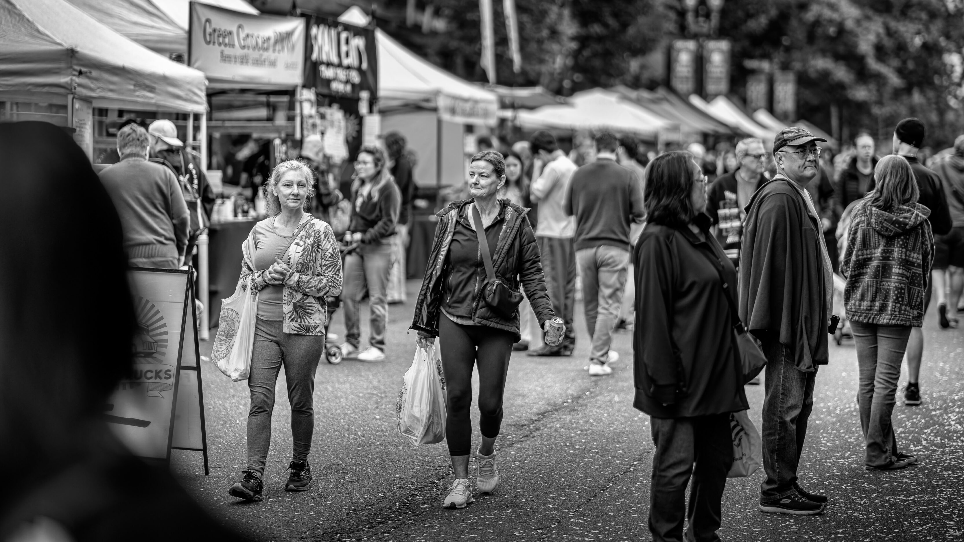 2026_09_19_Vancouver_85mm_0082-Edit-Edit_3840 ‣ In The Viewfinder People walk through a busy outdoor market with tents and stalls along a street, in grayscale.