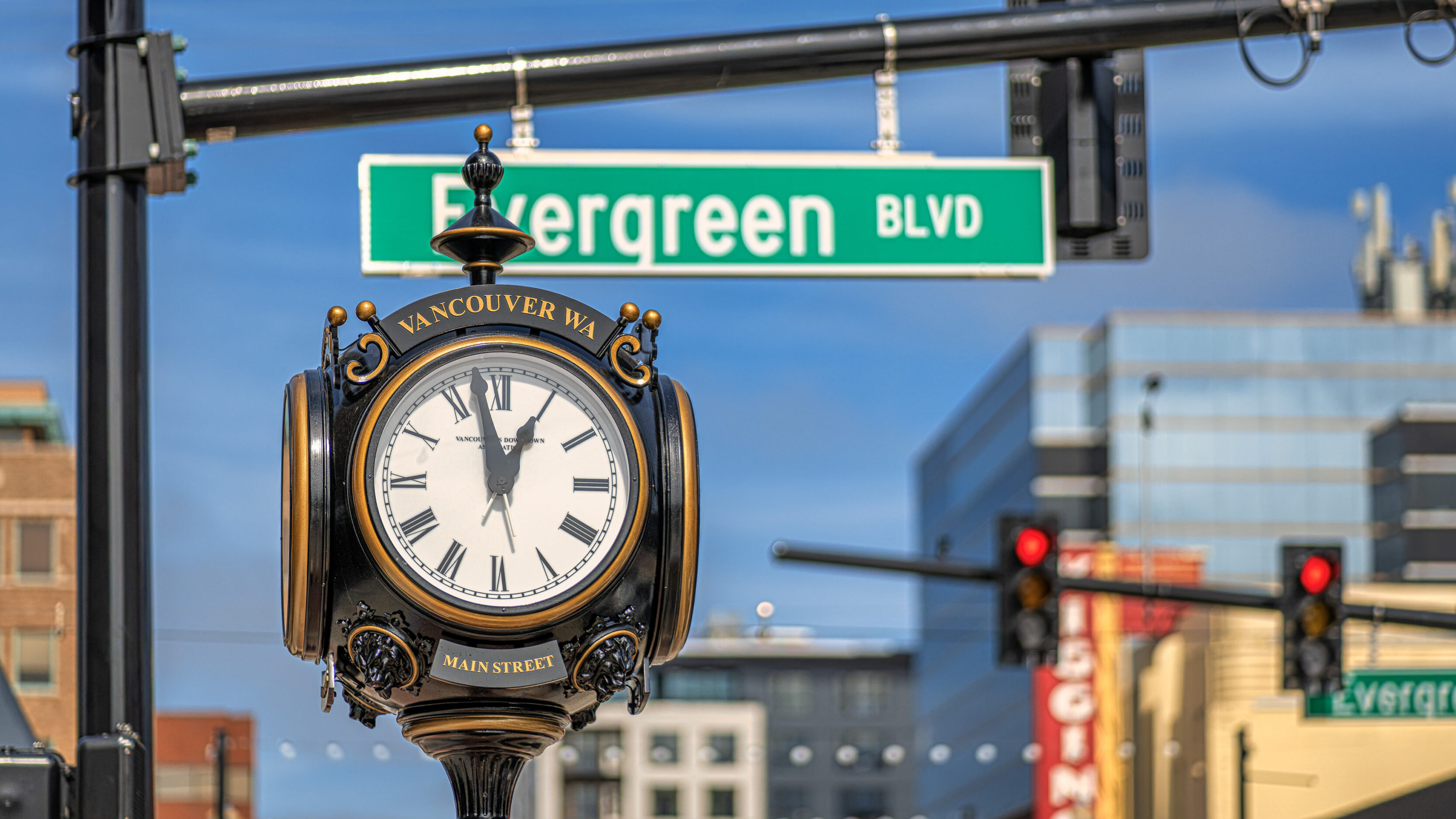 Decorative street clock reading'Main Street' under a green 'Evergreen Blvd' sign in Vancouver, WA with city buildings in the background