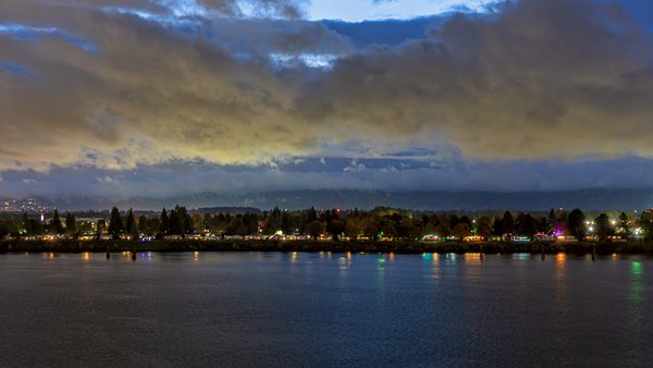 The View From Our Balcony 261026 Nighttime river scene with colorful lights reflecting on the water and a cloudy sky above.